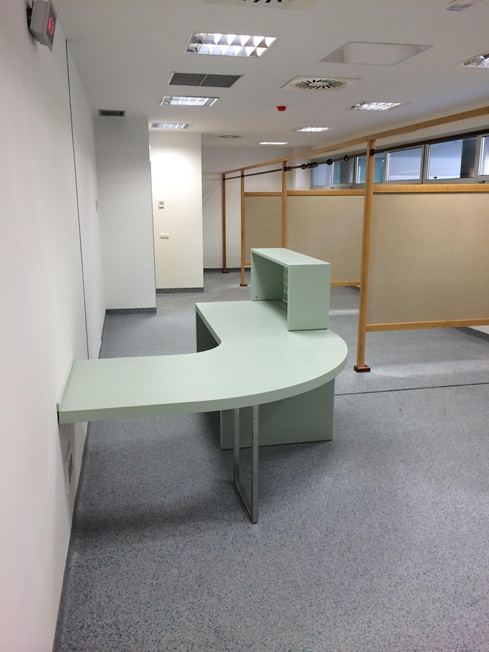 Diseño, fabricación y montaje de mostrador de recepción curvo con acabado en tono suave. Cuenta con un ala encastrada a la pared, estructura de apoyo metálica y un módulo superior para la atención al público