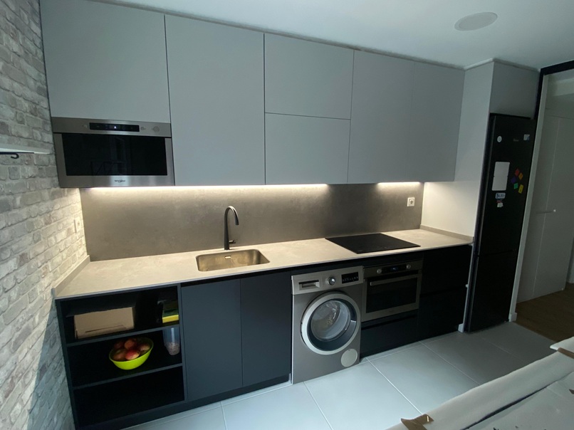 Cocina moderna sin tiradores con frentes en tono gris grafito y mate. Cuenta con iluminación LED integrada bajo muebles altos para un ambiente sofisticado