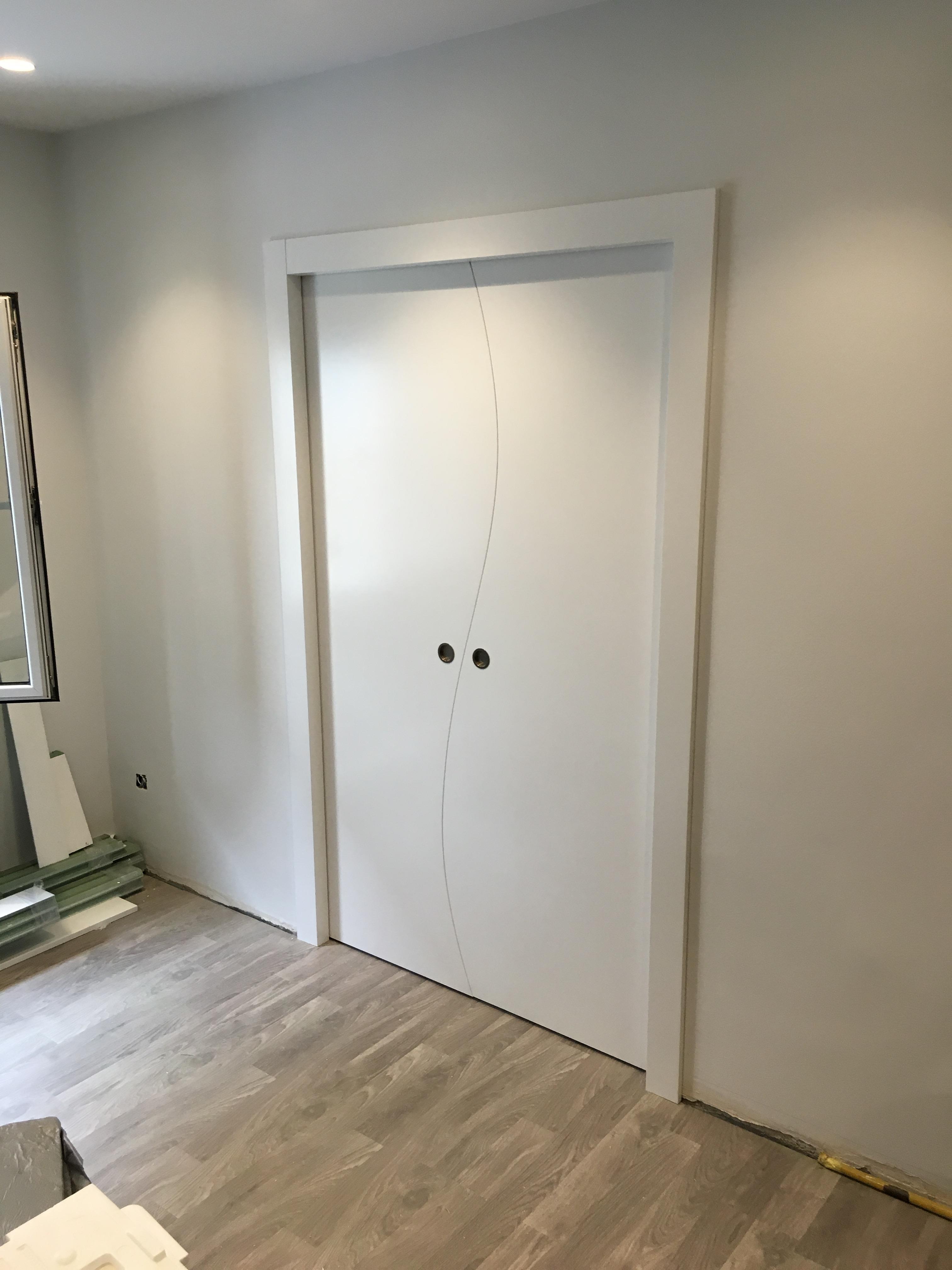 Puerta doble corredera de diseño exclusivo en acabado blanco mate, con junta orgánica curva y uñeros encastrados. Una solución sofisticada para dividir espacios con fluidez