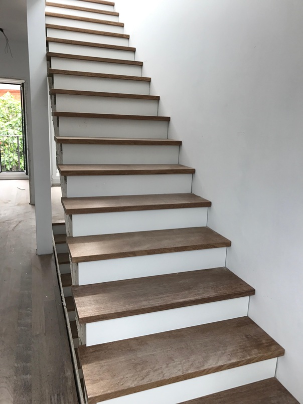 Escalera interior a medida peldaños de madera maciza con acabado natural y frontal lacado en blanco, adaptada perfectamente al espacio de la vivienda