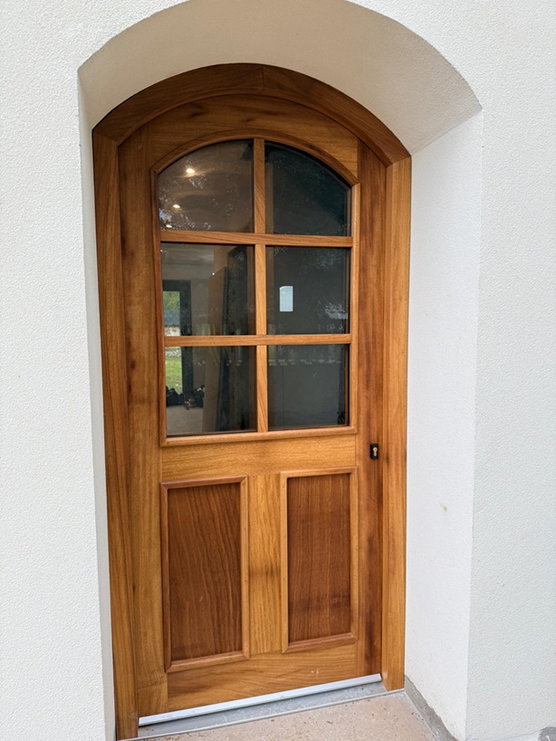 Adaptación perfecta a la arquitectura del edificio puerta acristalada con cabezal curvo en arco, aportando luz natural al recibidor y un toque distintivo a la fachada